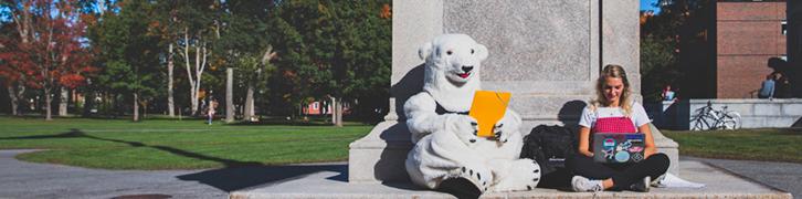 A Bowdoin student reads at the flagpole alongside the Polar Bear